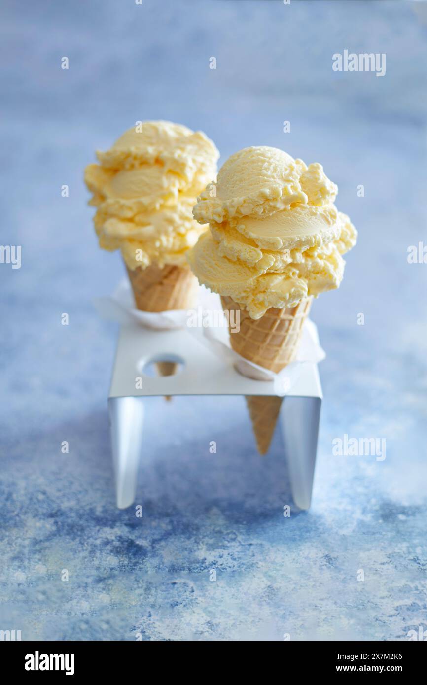 Gelato alla vaniglia in un cono, in un supporto per gelato bianco, su un dorso blu Foto Stock