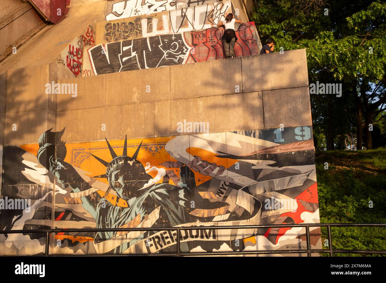 NEW YORK, NEW YORK - 20 MAGGIO: La gente siede una parte superiore della sporgenza alla base dell'Hells Gate Bridge (originariamente il New York Connecting Railroad Bridge) ad Astor Foto Stock