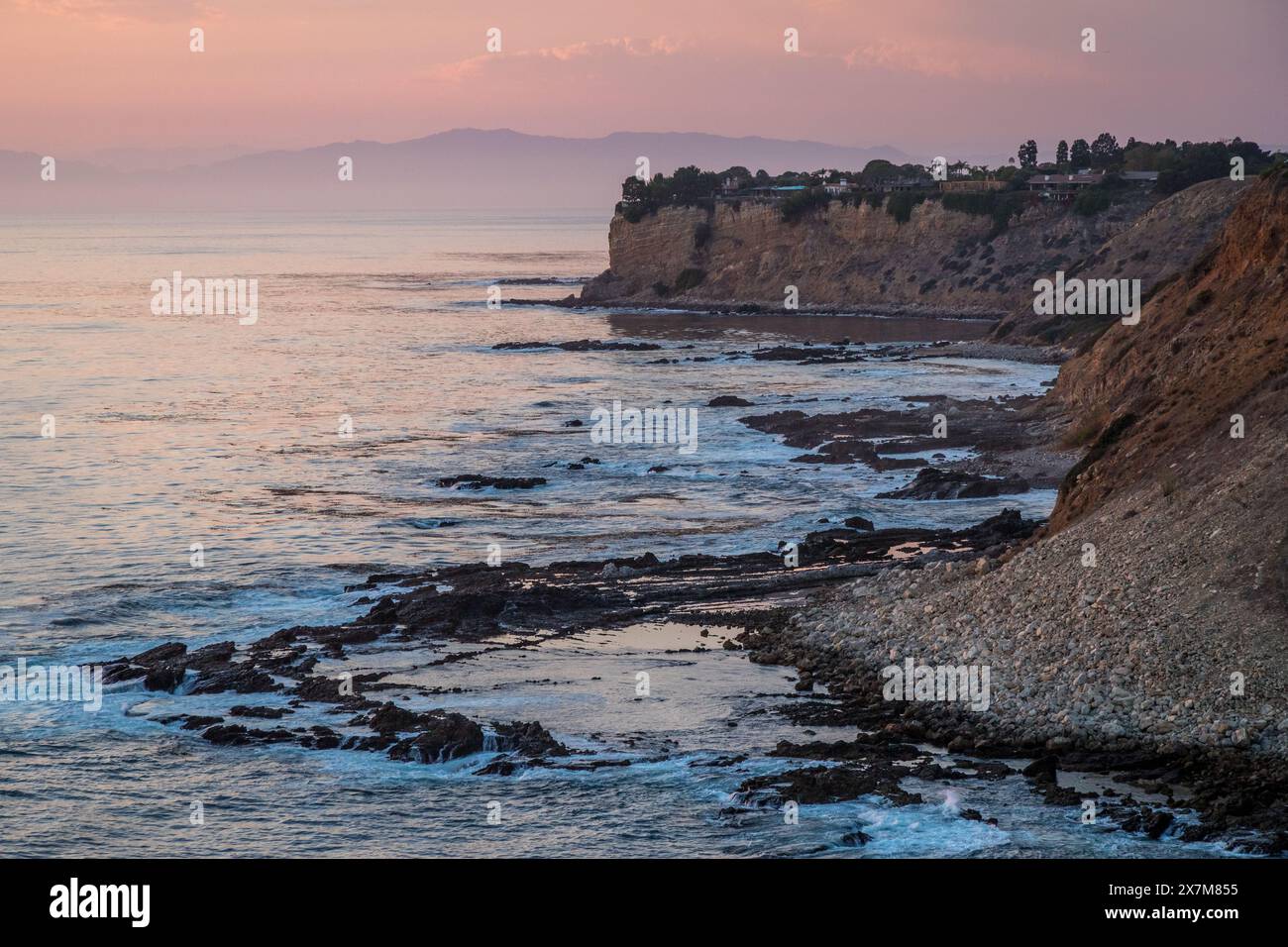 Mentre il sole tramonta sulla Golden Cove, le sue acque tranquille riflettono le calde sfumature del cielo, offrendo una fuga serena tra le aspre scogliere di Rancho Pa Foto Stock