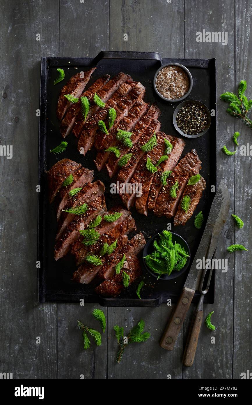Bistecca di manzo sul vassoio nero della griglia, raffinata con sale affumicato e punte fresche di abete rosso Foto Stock