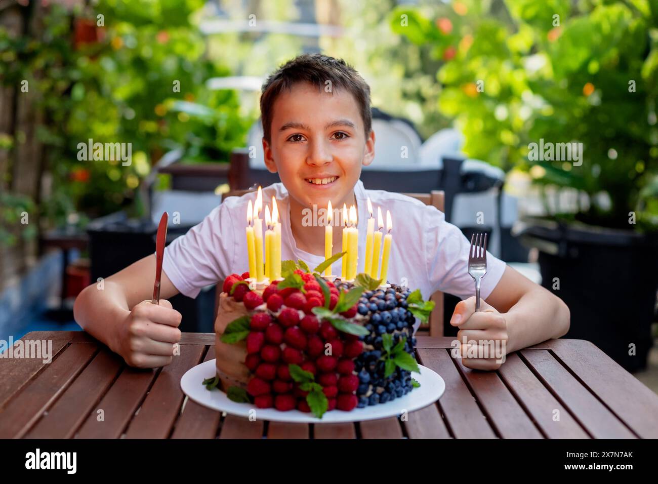 Un bambino di scuola carino che festeggia il suo compleanno a casa con i fratelli e la torta fatta in casa in giardino Foto Stock