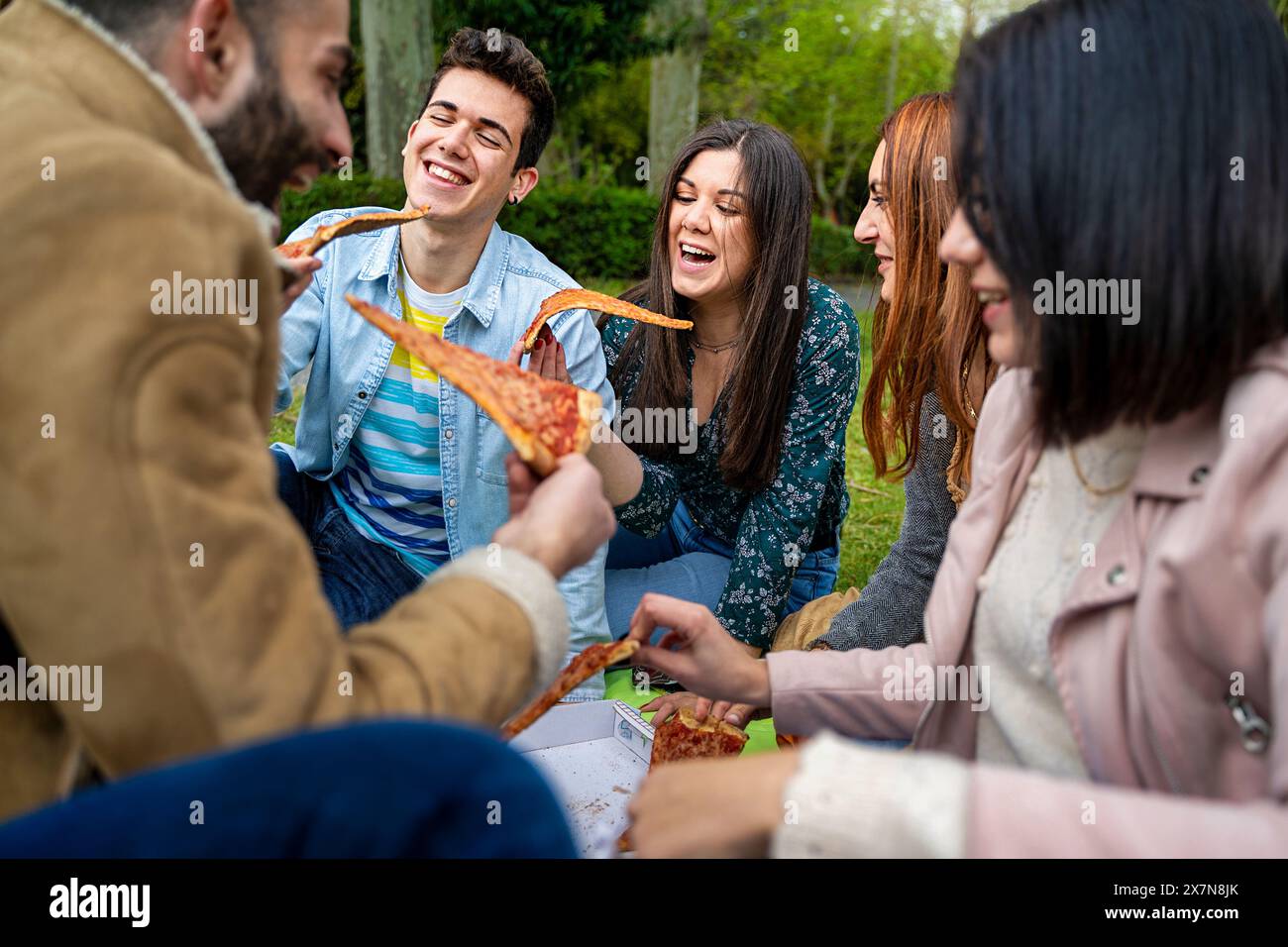 Gruppo di amici che mangiano pizza all'aperto - godendosi un momento di gioia e di socializzazione - ridendo e divertendosi - incontro informale, felicità e amicizia Foto Stock