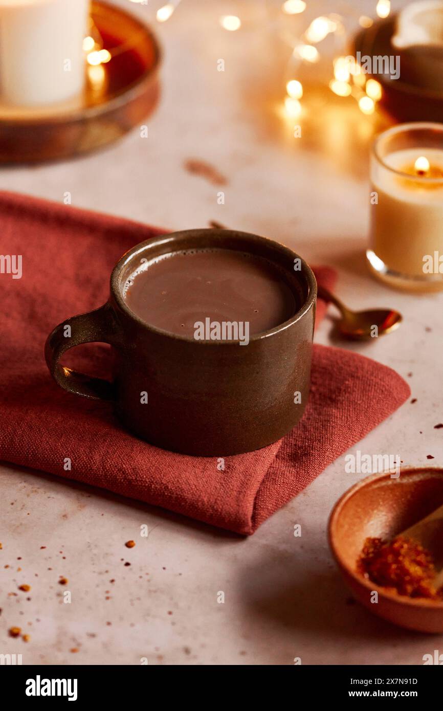 Cioccolata calda su un tovagliolo rosso con candele e cucchiaio Foto Stock