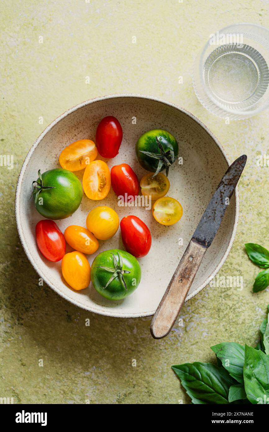 Ciotola di pomodori piccoli e colorati con un piccolo coltello su sfondo verde Foto Stock