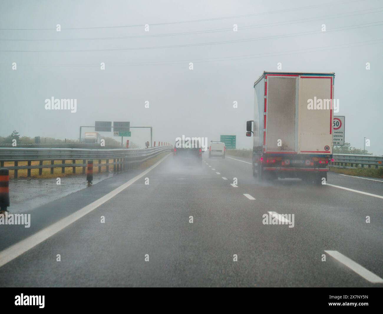 Piacenza, Italia - 22 aprile 2024 Una scena autostradale sotto un cielo coperto con auto e camion con segnaletica stradale e un cavalcavia, giornata di pioggia su Motorwa Foto Stock