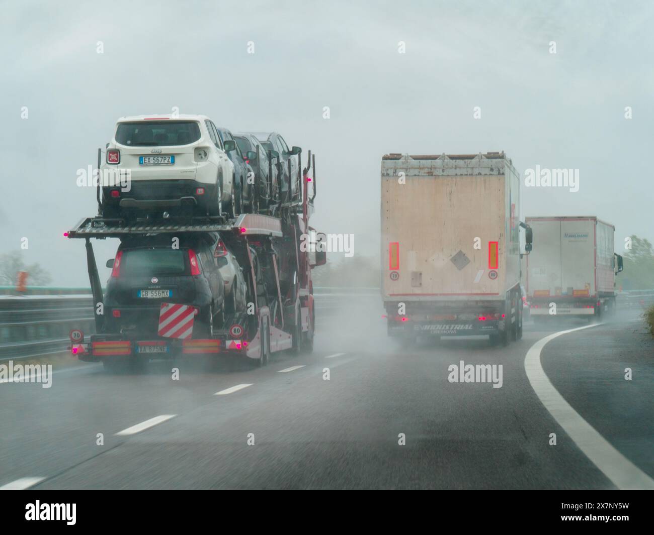 Piacenza, Italia - 22 aprile 2024 Una scena autostradale sotto un cielo coperto con auto e camion con segnaletica stradale e un cavalcavia, giornata di pioggia su Motorwa Foto Stock