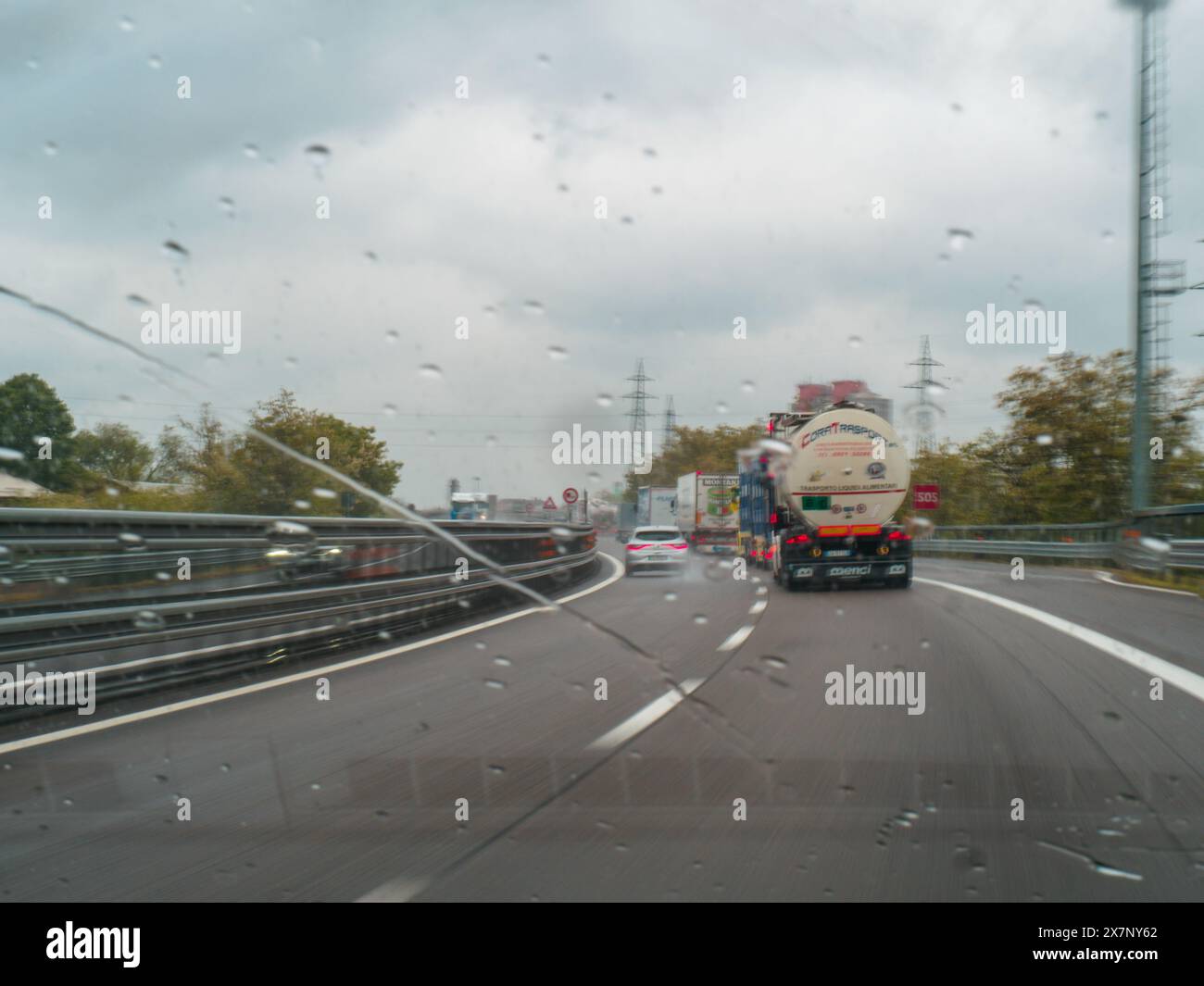 Piacenza, Italia - 22 aprile 2024 Una scena autostradale sotto un cielo coperto con auto e camion con segnaletica stradale e un cavalcavia, giornata di pioggia su Motorwa Foto Stock