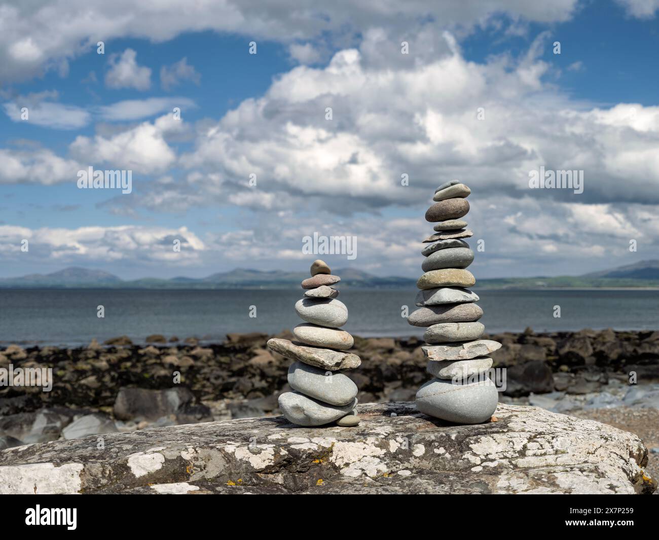 Pietre Zen bilanciate su una grande roccia su una spiaggia gallese in una splendida giornata primaverile con le montagne della penisola di Llyn e il mare sullo sfondo Foto Stock