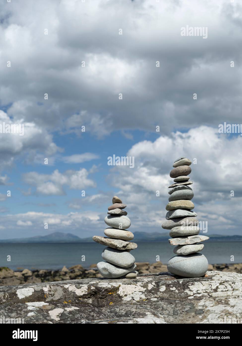 Pietre Zen bilanciate su una grande roccia su una spiaggia gallese in una splendida giornata primaverile con le montagne della penisola di Llyn e il mare sullo sfondo Foto Stock