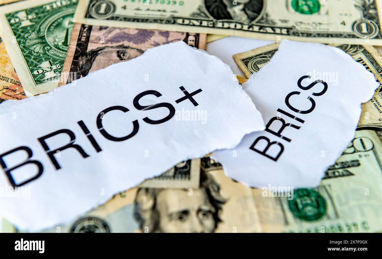 Un concetto di dedollarizzazione con le parole BRICS e BRICS+ in cima a una pila di banconote in dollari USA. Foto Stock