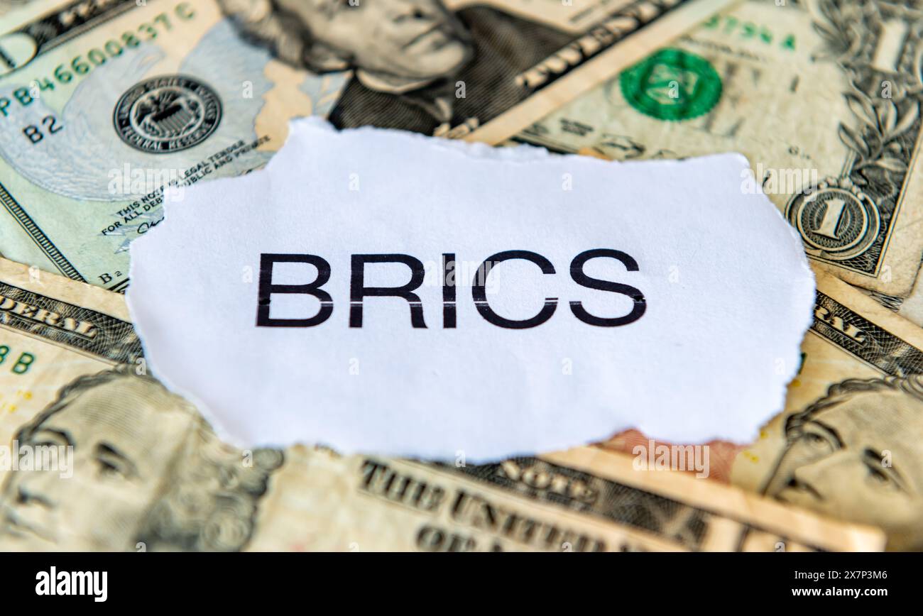 Un concetto di dedollarizzazione con i BRICS in cima a una pila di banconote in dollari americani. Foto Stock