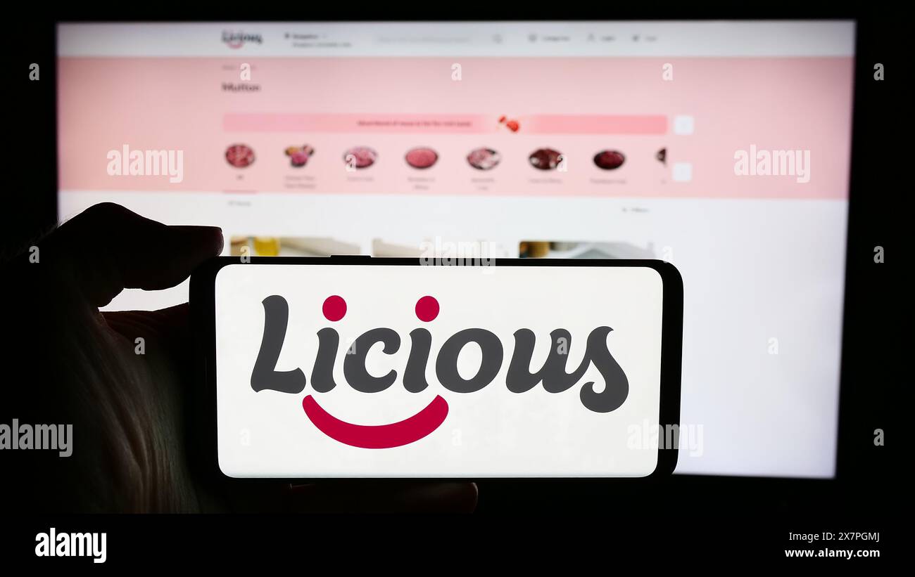 Persona che tiene un cellulare con il logo della società indiana di consegna di cibo Licious davanti alla pagina web aziendale. Mettere a fuoco il display del telefono. Foto Stock