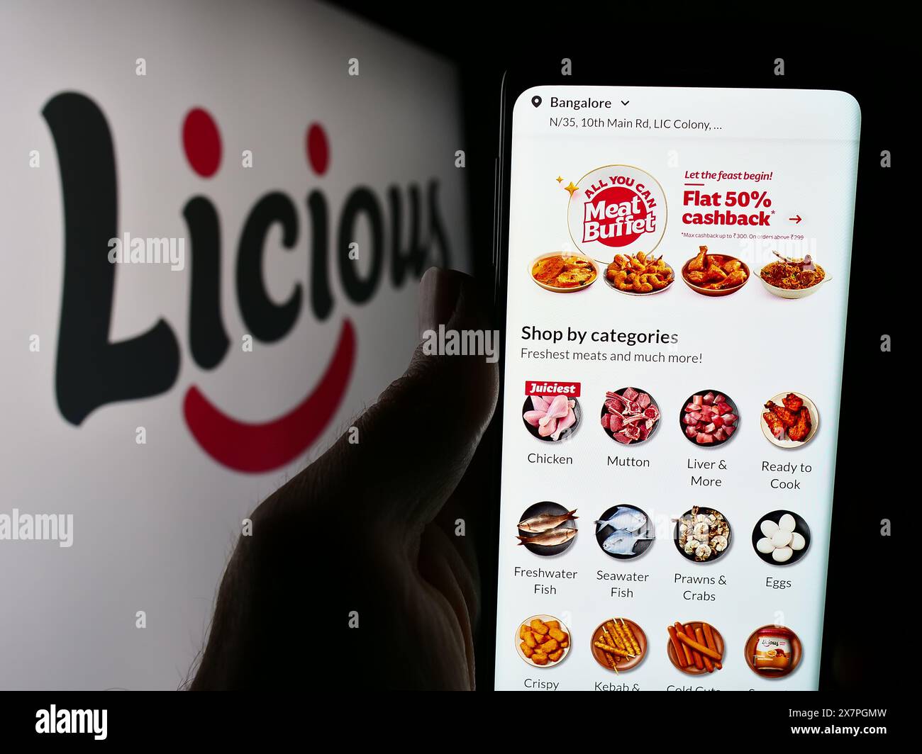 Persona con smartphone e sito web della società indiana Licious, che si occupa della fornitura di prodotti alimentari, davanti al logo aziendale. Messa a fuoco al centro del display del telefono. Foto Stock