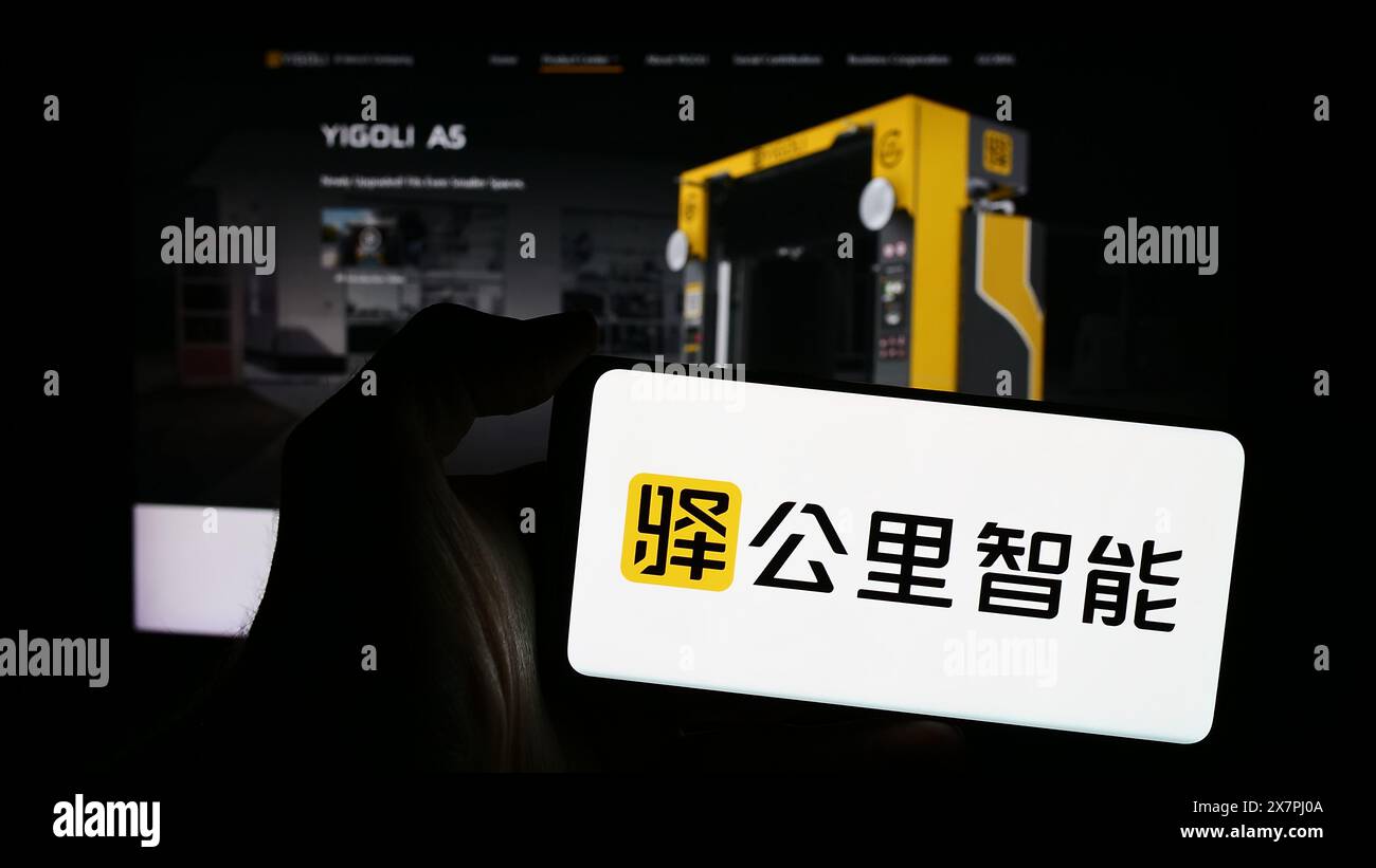Persona che detiene un telefono cellulare con il logo della società tecnologica cinese Yigongli Intelligence (1KMXC) di fronte alla pagina web. Mettere a fuoco il display del telefono. Foto Stock