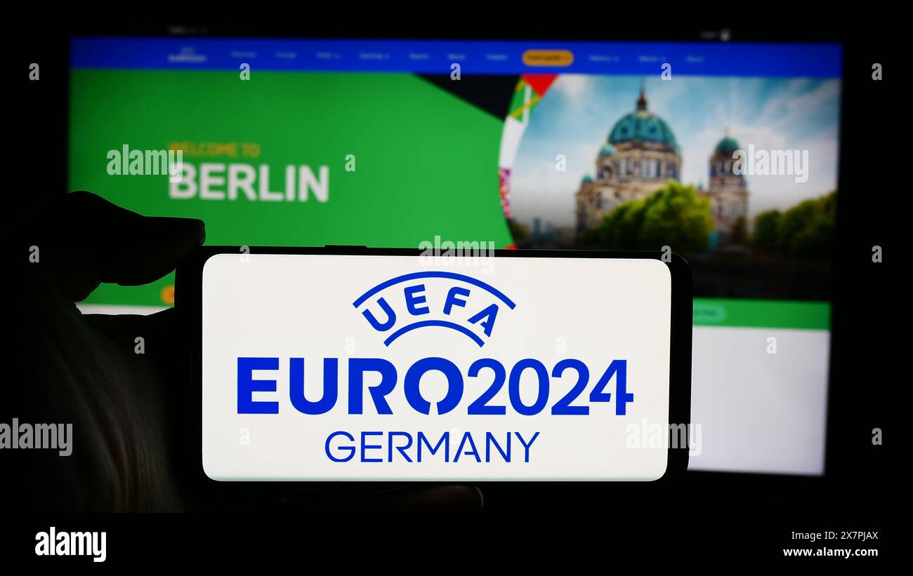 Persona che detiene un cellulare con logo del campionato europeo di calcio UEFA Euro 2024 davanti alla pagina web. Mettere a fuoco il display del telefono. Foto Stock