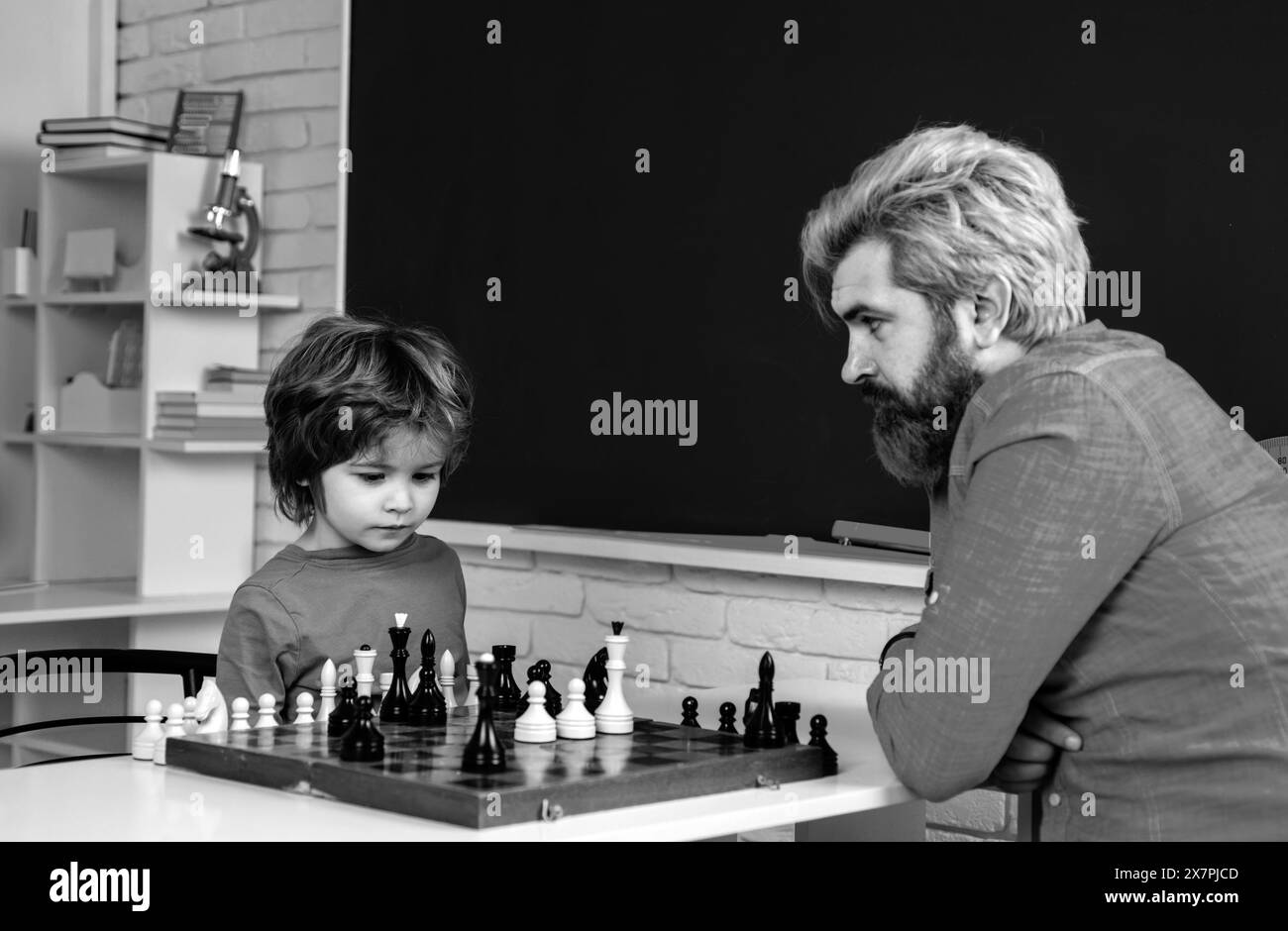 Tutor di casa che aiuta ragazzo con gli scacchi. Un bambino felice che gioca a scacchi con un anziano a casa. Foto Stock