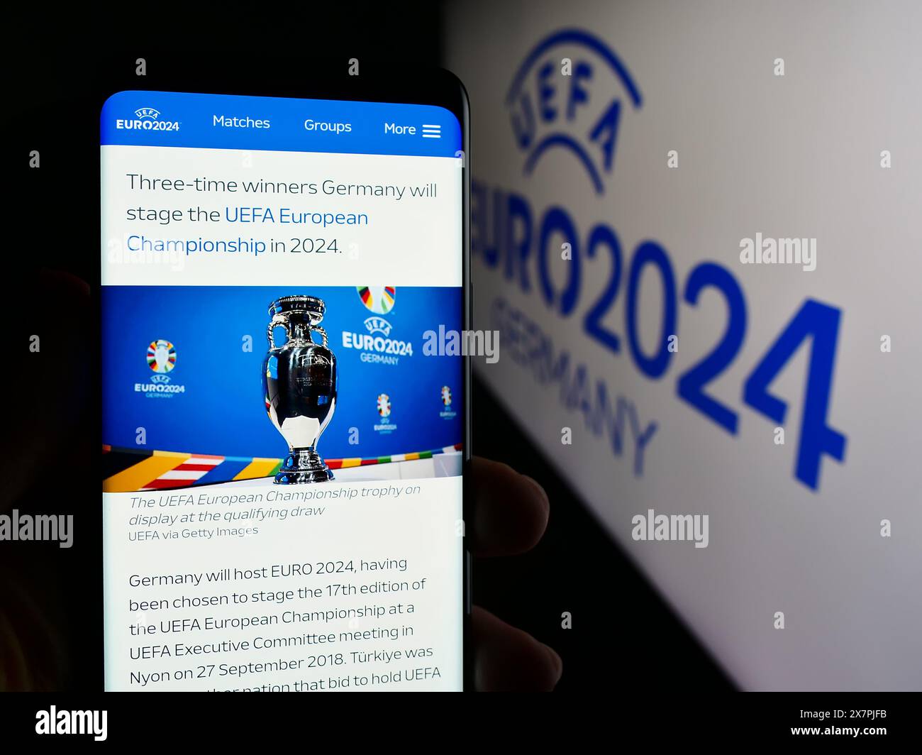 Persona che detiene un cellulare con pagina web del campionato europeo di calcio UEFA Euro 2024 davanti al logo. Messa a fuoco al centro del display del telefono. Foto Stock