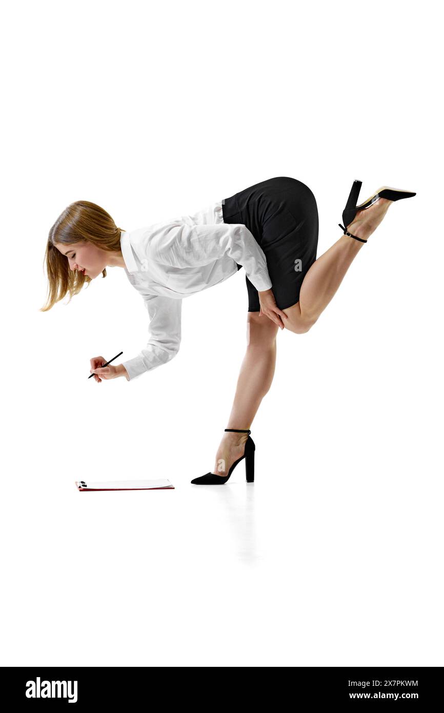 Donna d'affari elegantemente vestita che si piega in avanti per scrivere su appunti collocati sul pavimento su sfondo bianco studio. Foto Stock