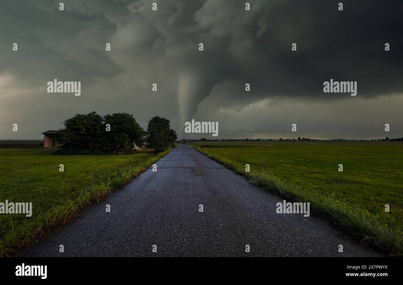 Strada di campagna attraverso campi con sfondo tornado lontano. Foto Stock