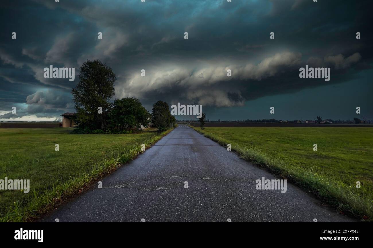 Strada di campagna attraverso campi con sfondo tornado lontano. Foto Stock