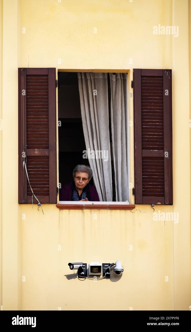 Donna anziana alla finestra che guarda la strada, che agisce come telecamera di sorveglianza umana Foto Stock