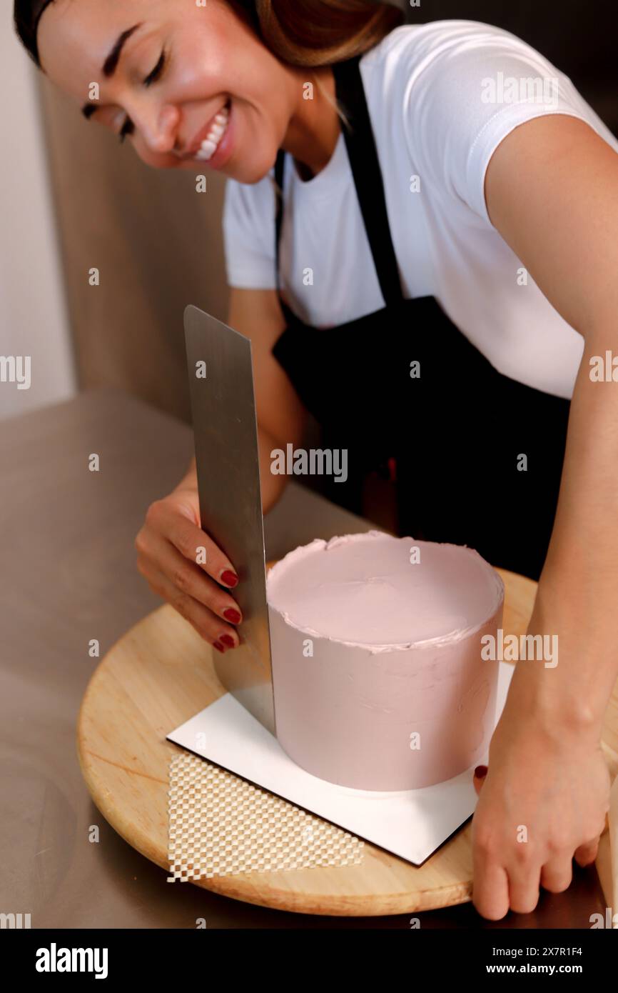Una donna deliziata in un abbigliamento casual applica meticolosamente la glassa a una torta, mostrando esperienza e gioia nel forno Foto Stock