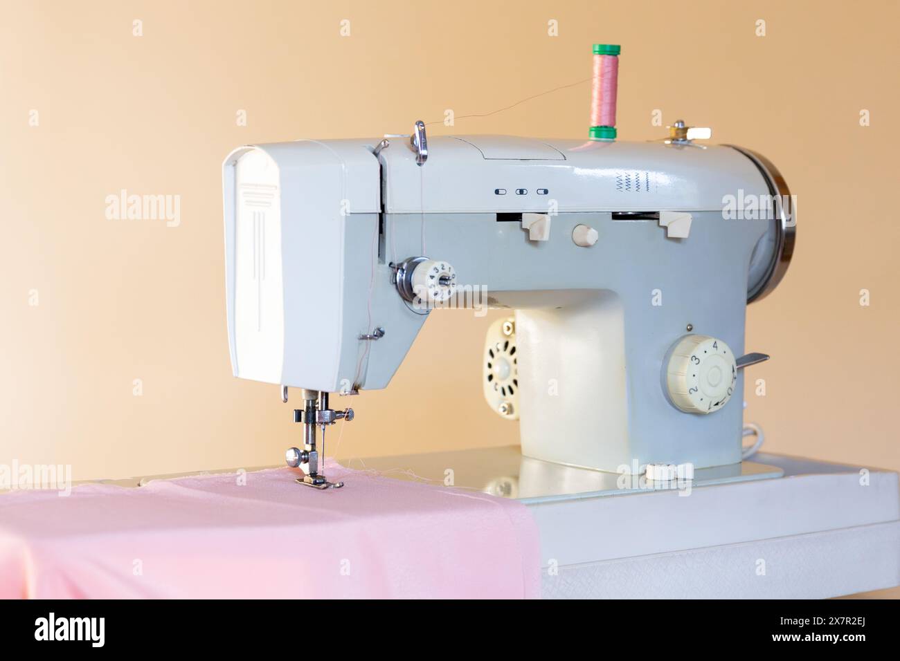 Una macchina da cucire industriale con un rocchetto di filetto verde su un tavolo rivestito di tessuto, pronta per essere realizzata in un'officina di design Foto Stock