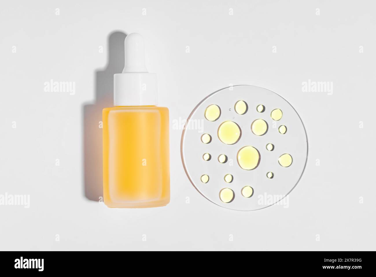 Stesa piatta di un flacone contagocce per siero cosmetico con siero giallo accanto alle gocce del campione su una superficie bianca, per un'estetica pulita e minimalista per lo sci Foto Stock