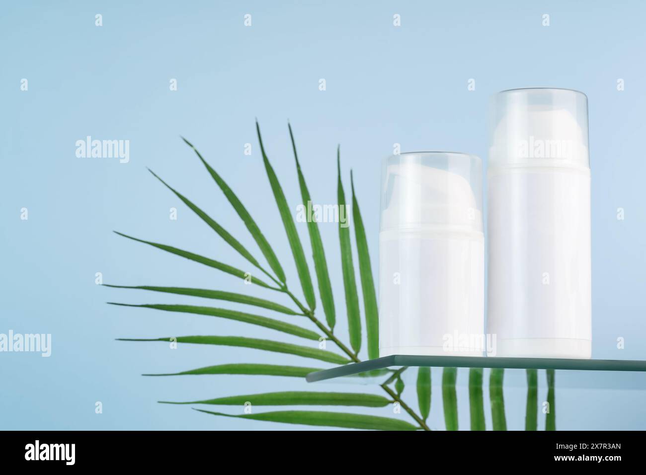 Tubi cosmetici bianchi vuoti, ideali per modelli di mockup, completati da una foglia verde tropicale su uno sfondo blu sereno. Foto Stock