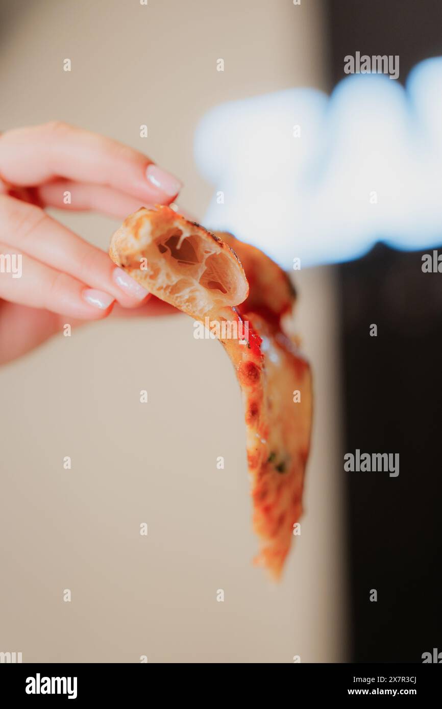 Una persona anonima e corta che tiene una fetta di pizza a buon mercato, mostrando piatti della pizzeria Foto Stock