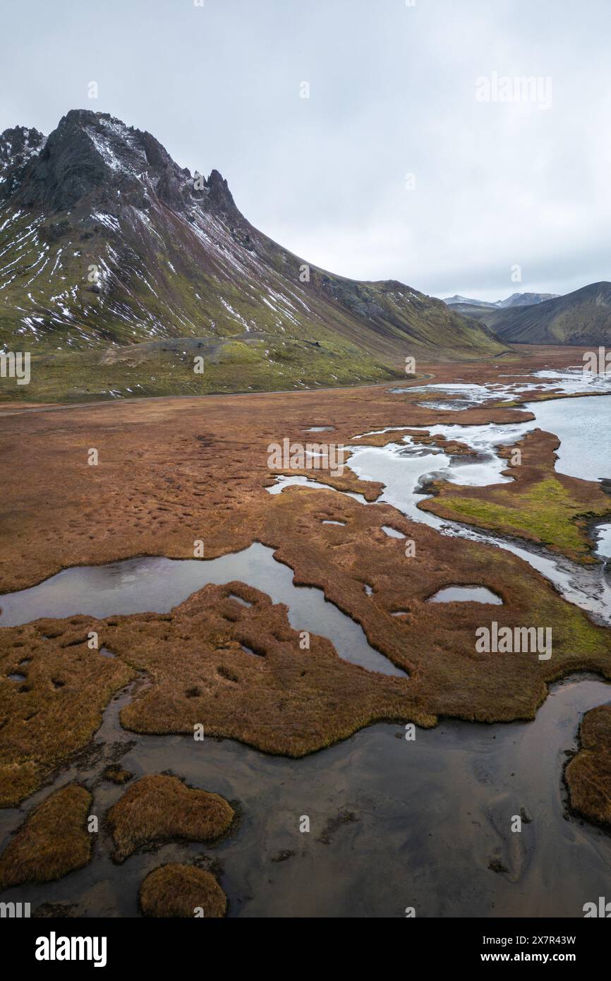 Una splendida vista aerea degli altopiani con una maestosa vetta di montagna e un torrente serpeggiante, circondato da un paesaggio remoto e tranquillo Foto Stock