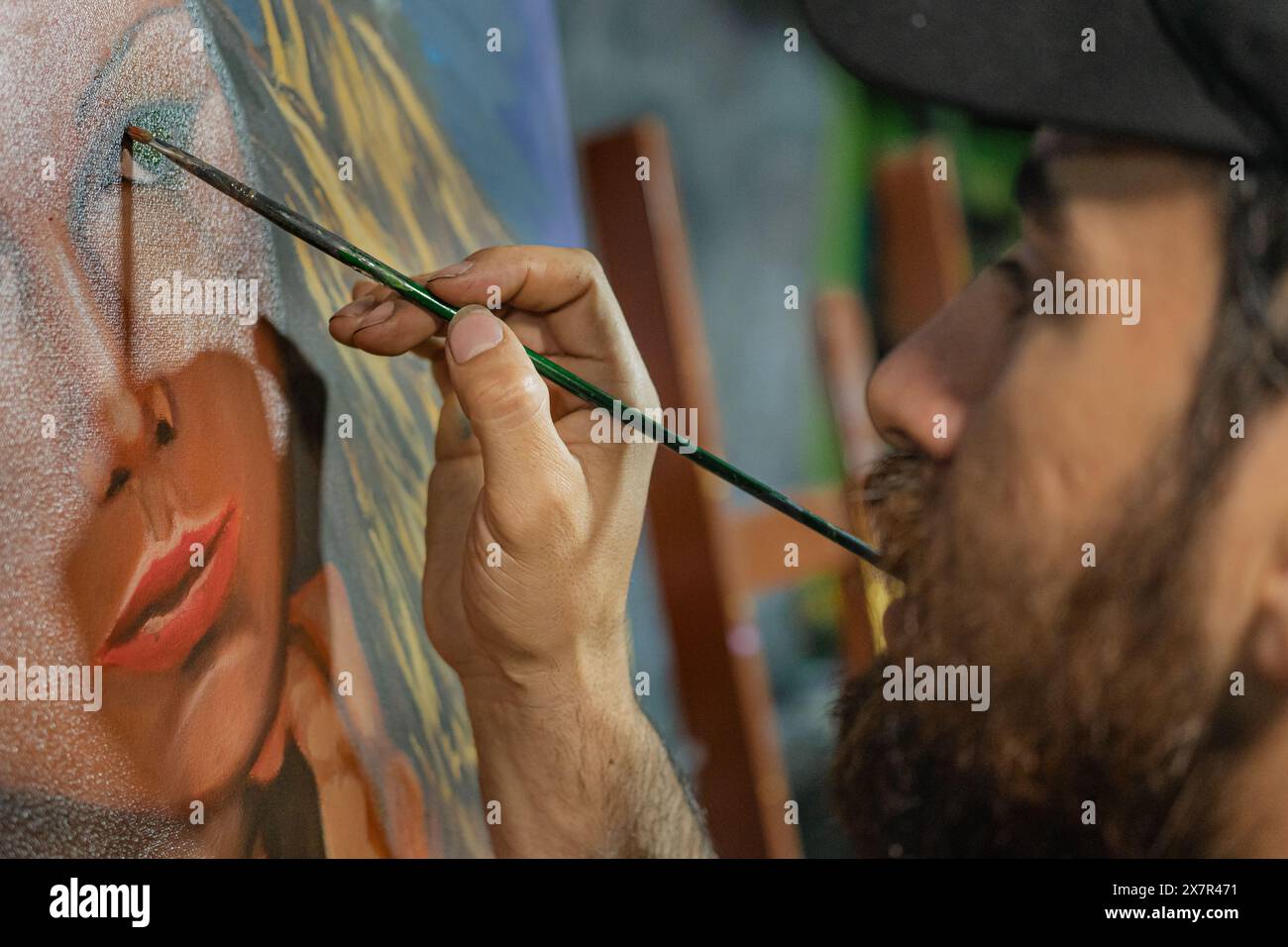 Un artista latinoamericano descrive con attenzione le labbra di una donna su una tela nel suo accogliente studio. Foto Stock