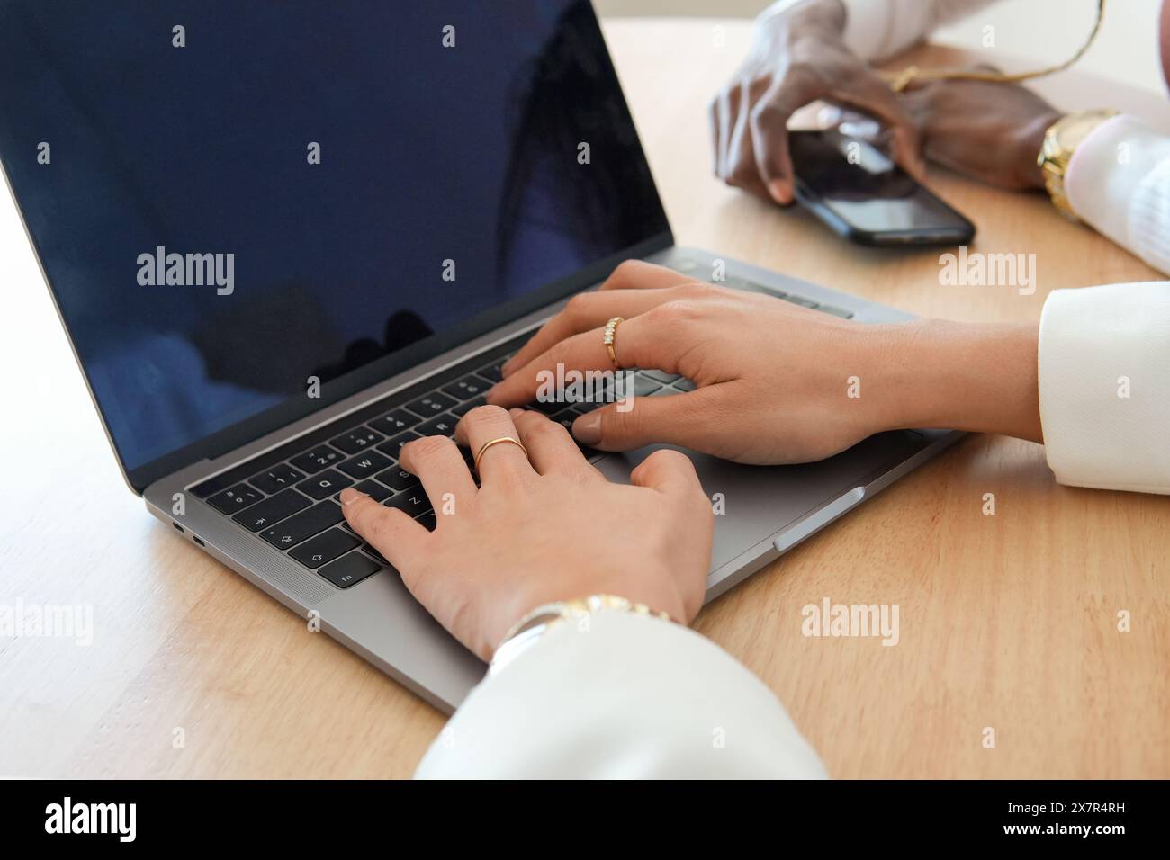 Vista ravvicinata di due donne che lavorano insieme su una scrivania di legno, una che digita su un computer portatile, l'altra utilizza uno smartphone e un mouse la loro messa a fuoco indica Foto Stock