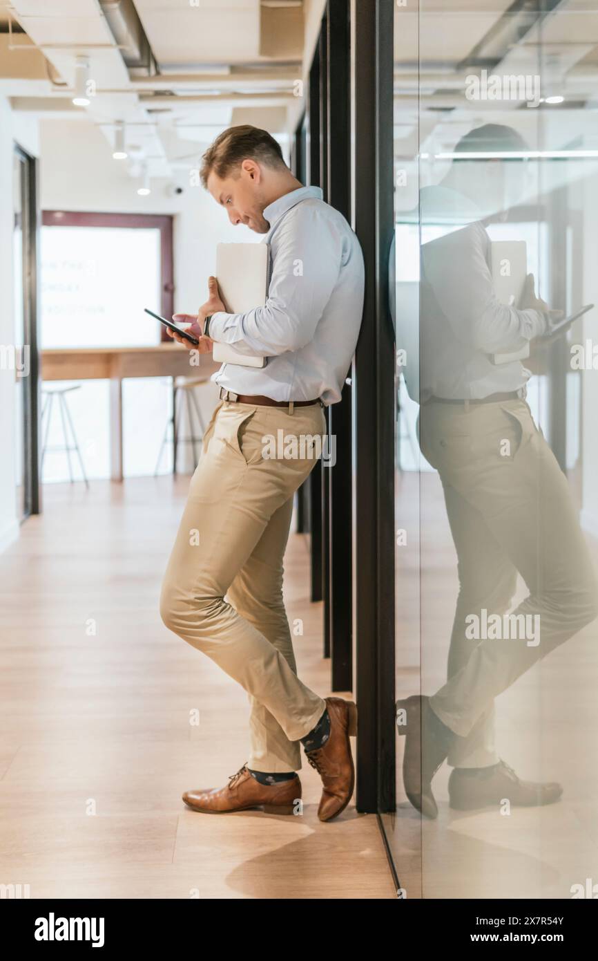 Un giovane professionista attento utilizza un tablet digitale nel corridoio di un moderno ufficio di coworking, che riflette la flessibilità del lavoro moderno Foto Stock