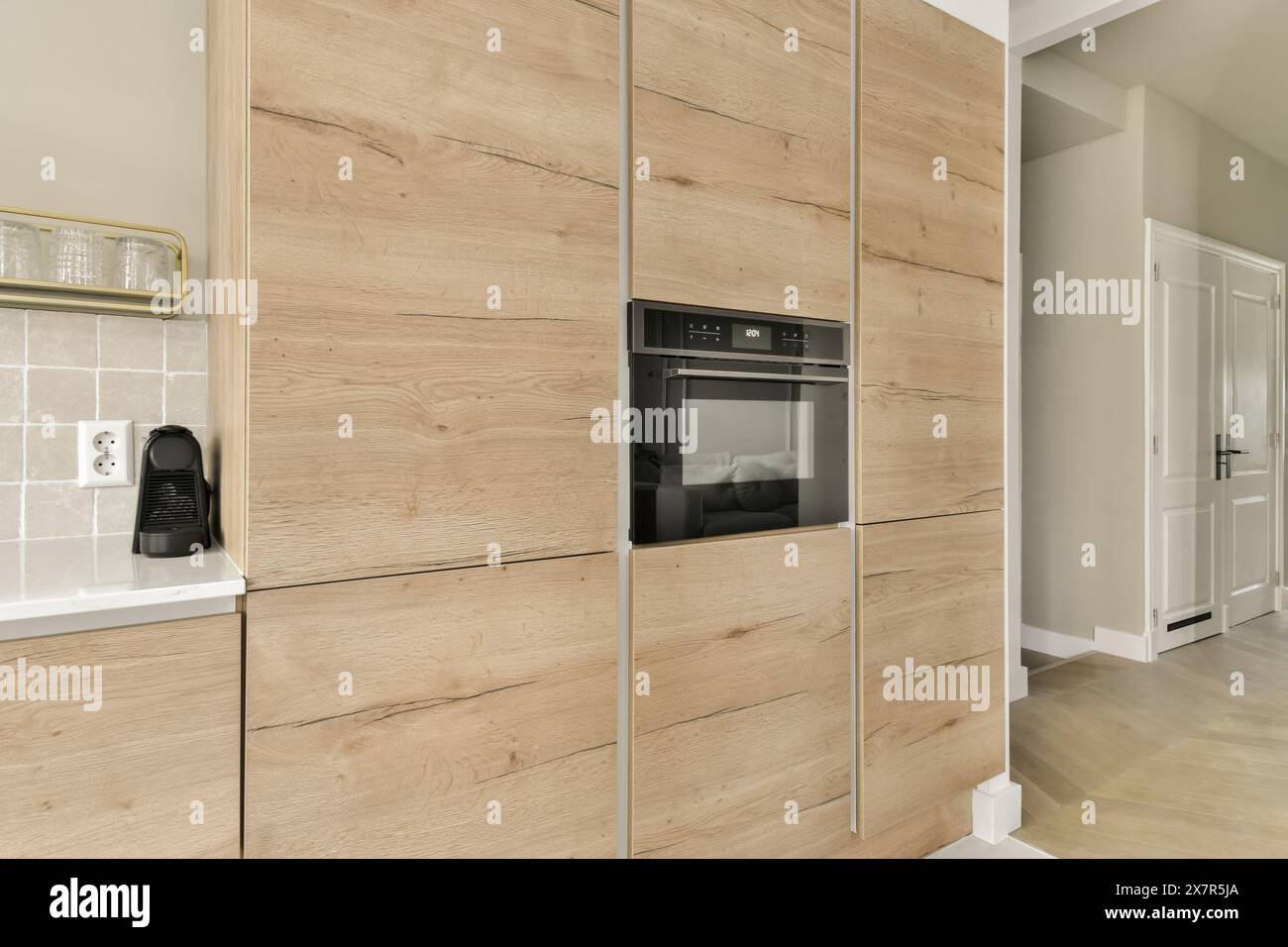 Una cucina di stile contemporaneo con forno a incasso con pannelli di legno chiaro, completata da piastrelle bianche e un design minimalista Foto Stock