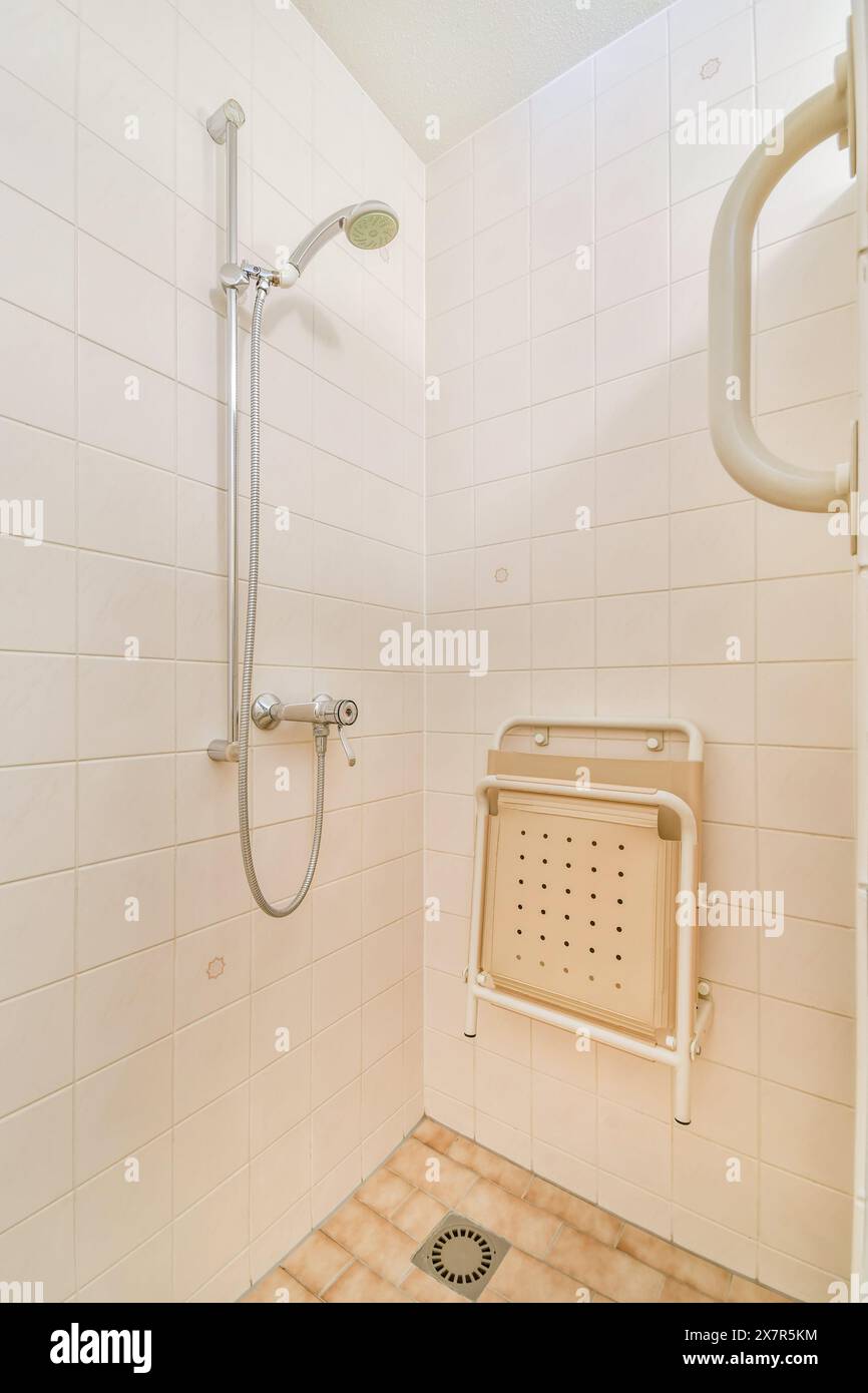 Cabina doccia accessibile con sedia a rotelle, pulita e ben tenuta, dotata di soffione per doccia portatile, barra regolabile e sedile pieghevole per una maggiore comodità e sicurezza Foto Stock