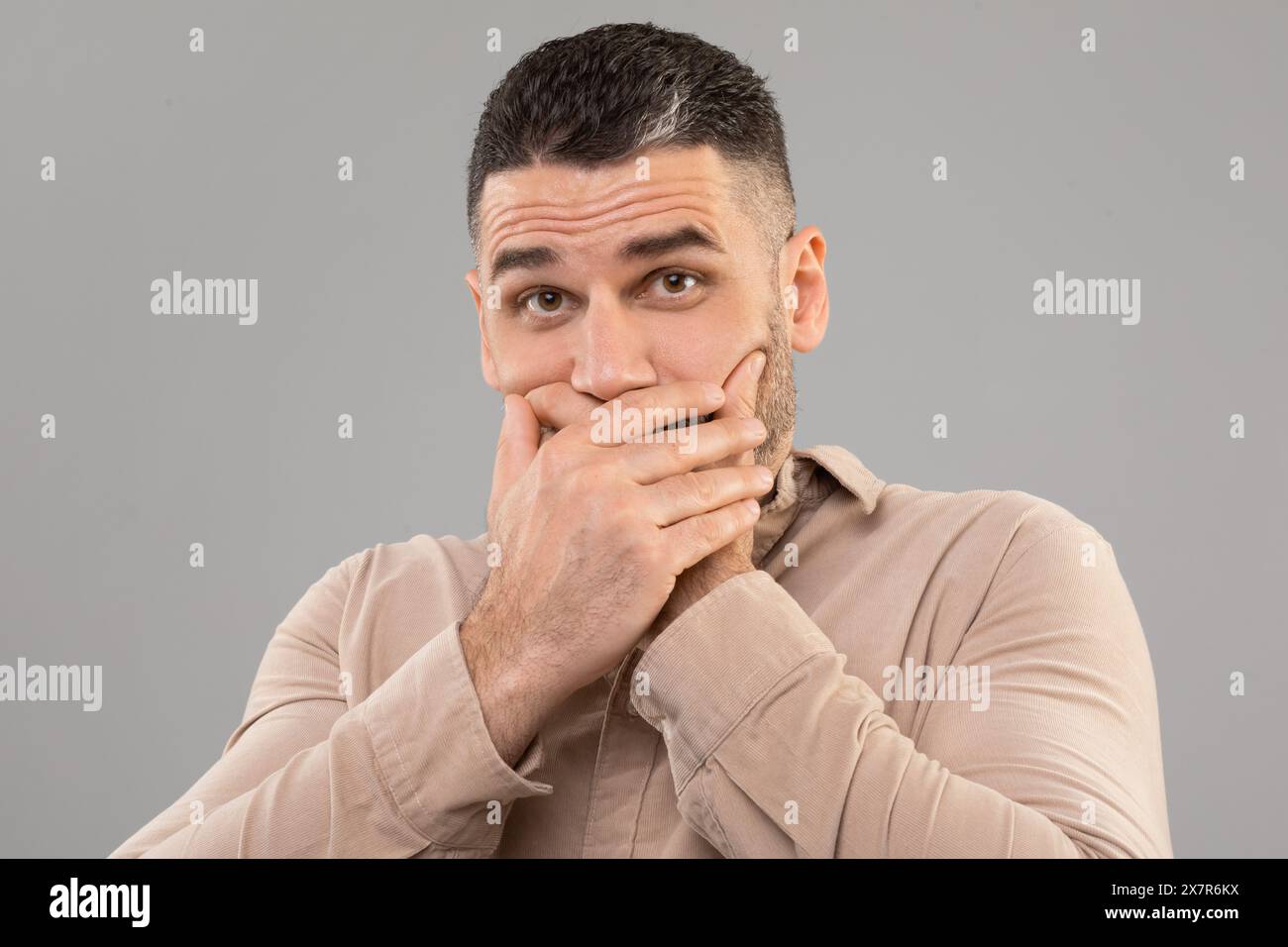 L'uomo copre la bocca con le mani, sfondo grigio Foto Stock