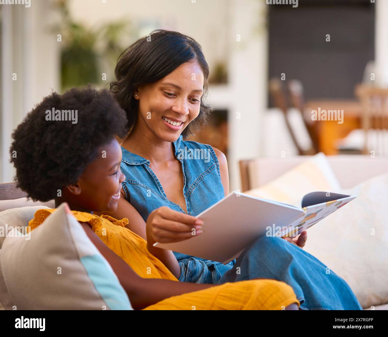 Famiglia con madre e figlia seduti sul divano a casa lettura Prenota insieme Foto Stock