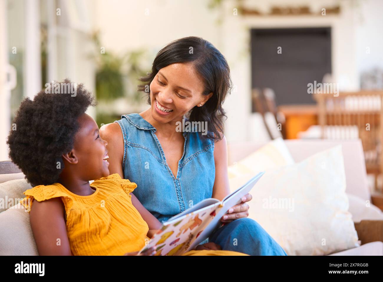 Famiglia con madre e figlia seduti sul divano a casa lettura Prenota insieme Foto Stock