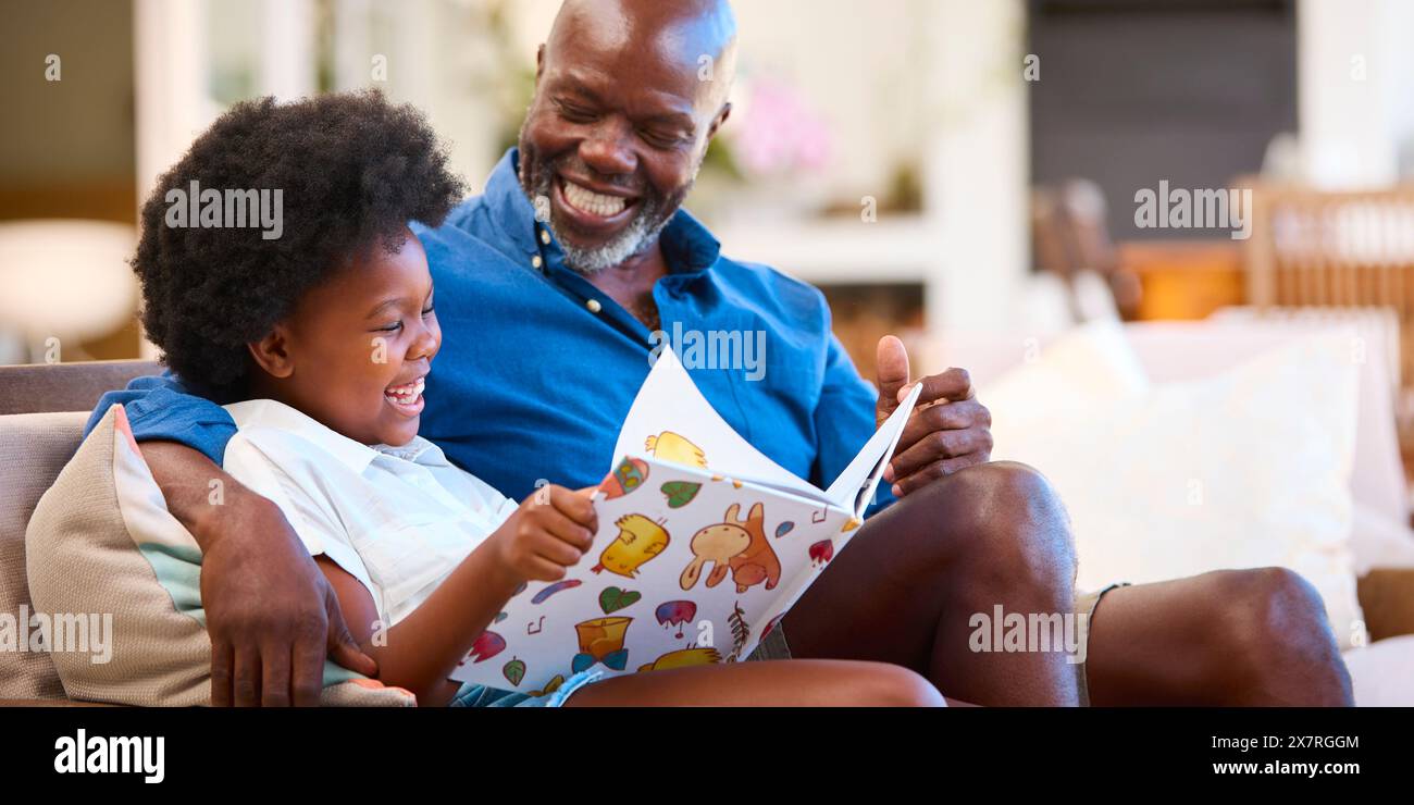 Famiglia con nonno e nipote seduti sul divano a Home Reading Book insieme Foto Stock