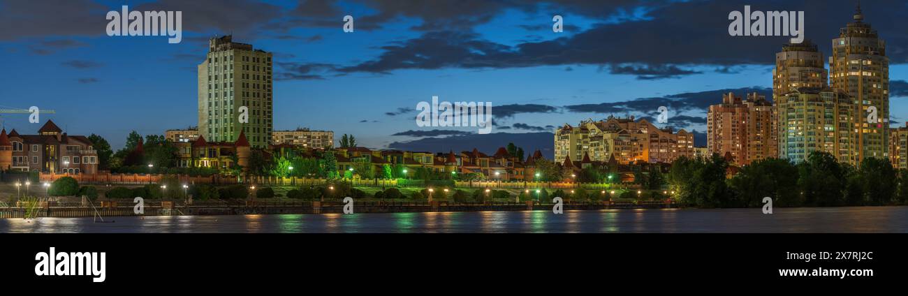 Sagome di case al tramonto sull'argine illuminato del fiume Dnieper sullo sfondo di un cielo stellato e della luna con nuvole di luce. Foto Stock