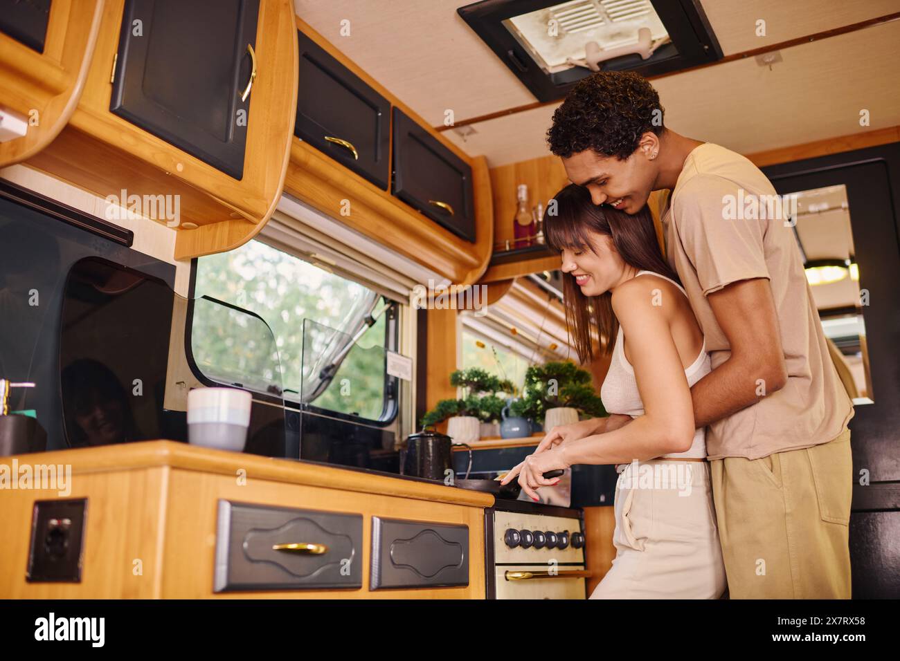 Una coppia interrazziale sta insieme in una cucina accogliente, condividendo un momento di intimità e collaborazione mentre preparano un pasto. Foto Stock