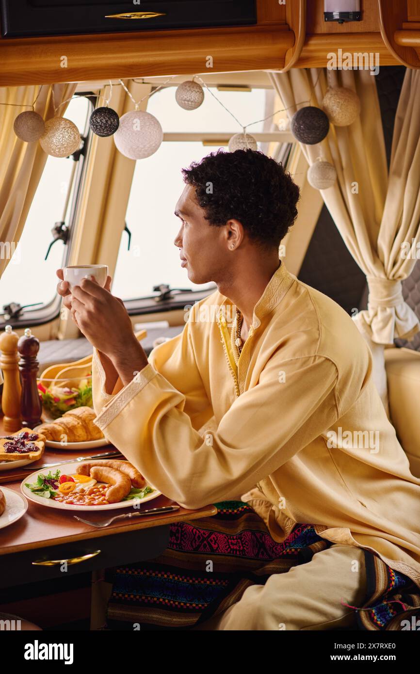 Un uomo gode di un momento di relax mentre siede a un tavolo con una tazza di caffè. Foto Stock