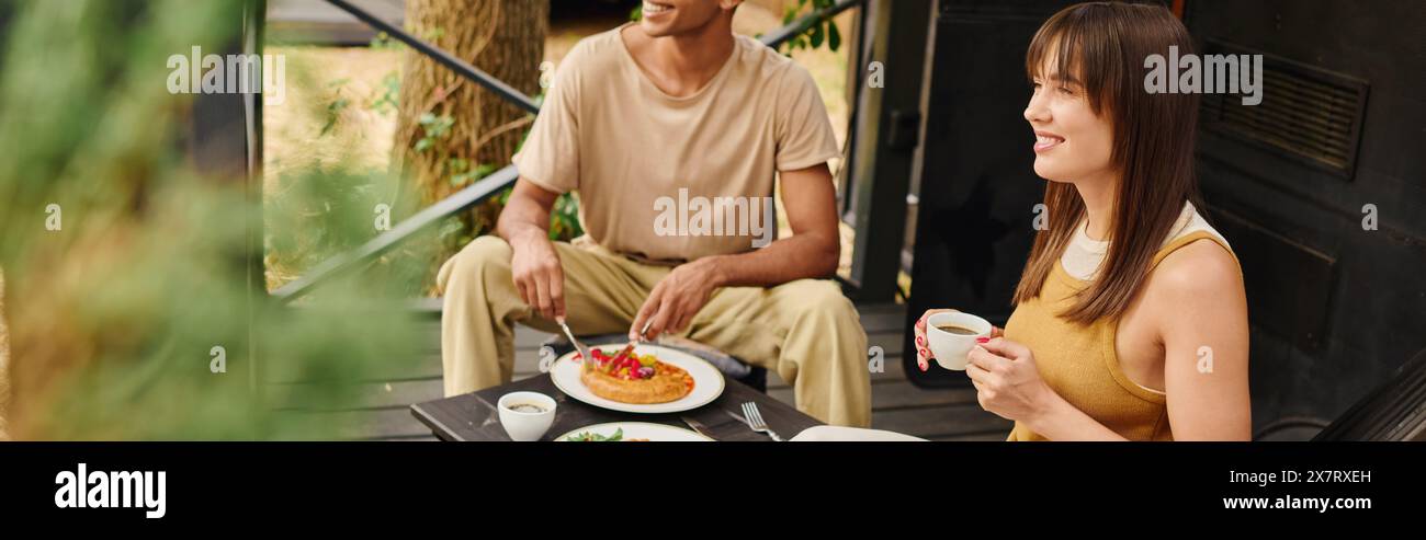 Una coppia interrazziale che gusta un pasto insieme a un tavolo pieno di cibo delizioso, condividendo un momento romantico in un camper. Foto Stock