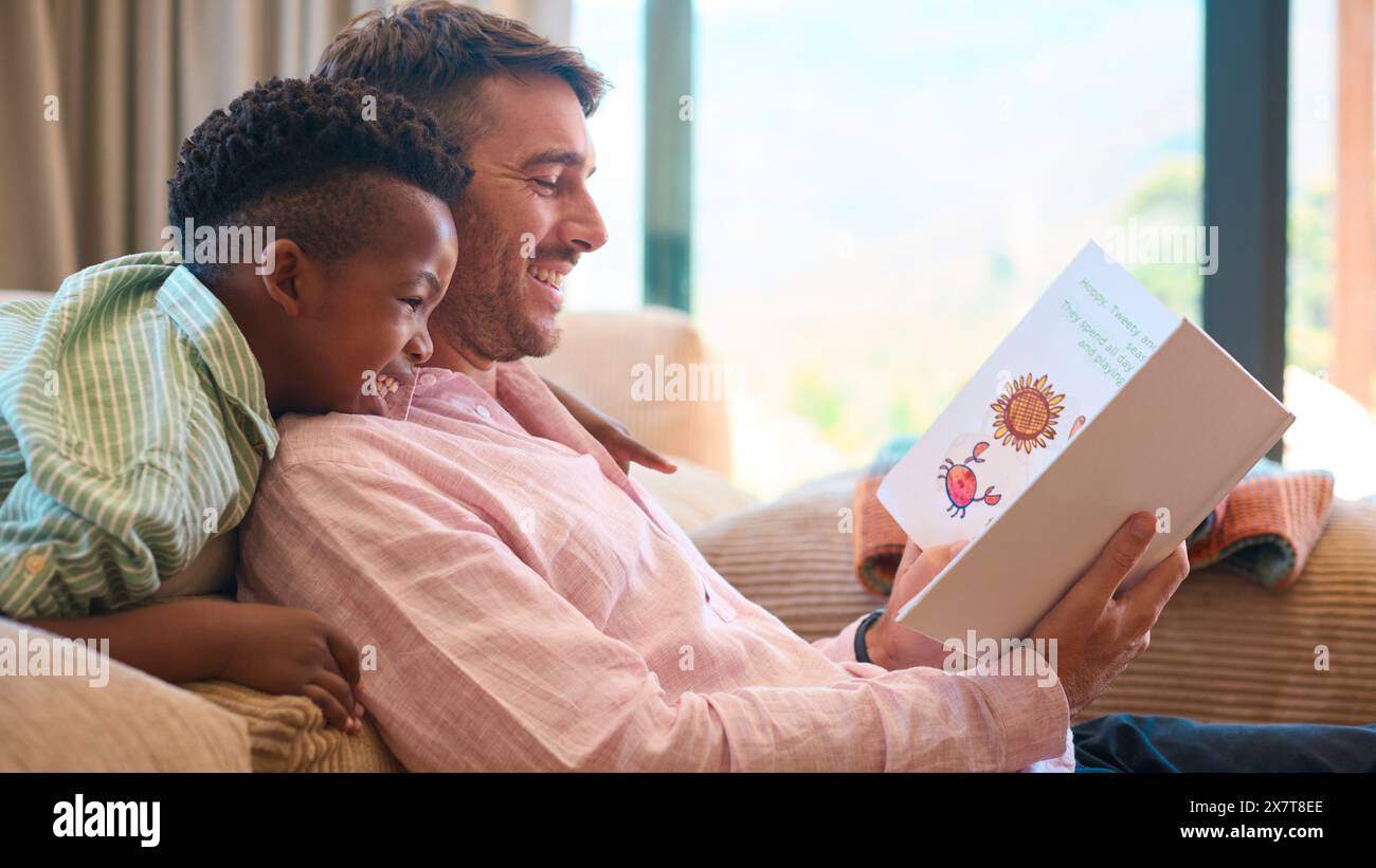 Multi Racial Family at Home con padre e figlio che leggono insieme il libro Foto Stock