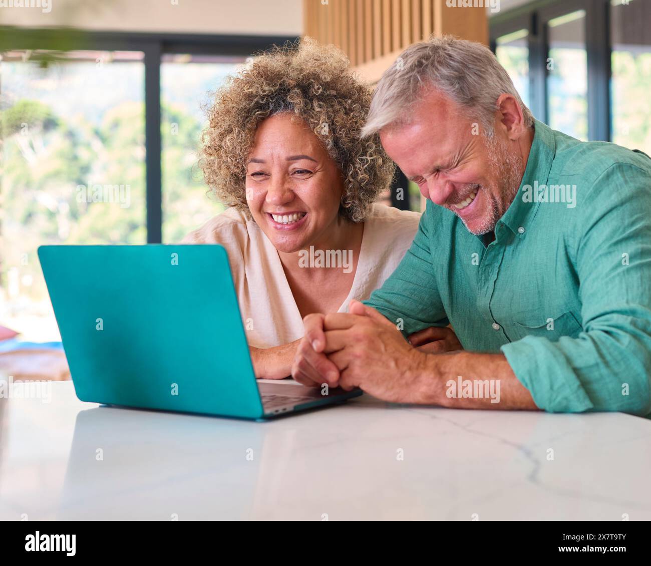 Maturo coppia multi-razziale a casa che celebra le buone notizie Looking At laptop Foto Stock