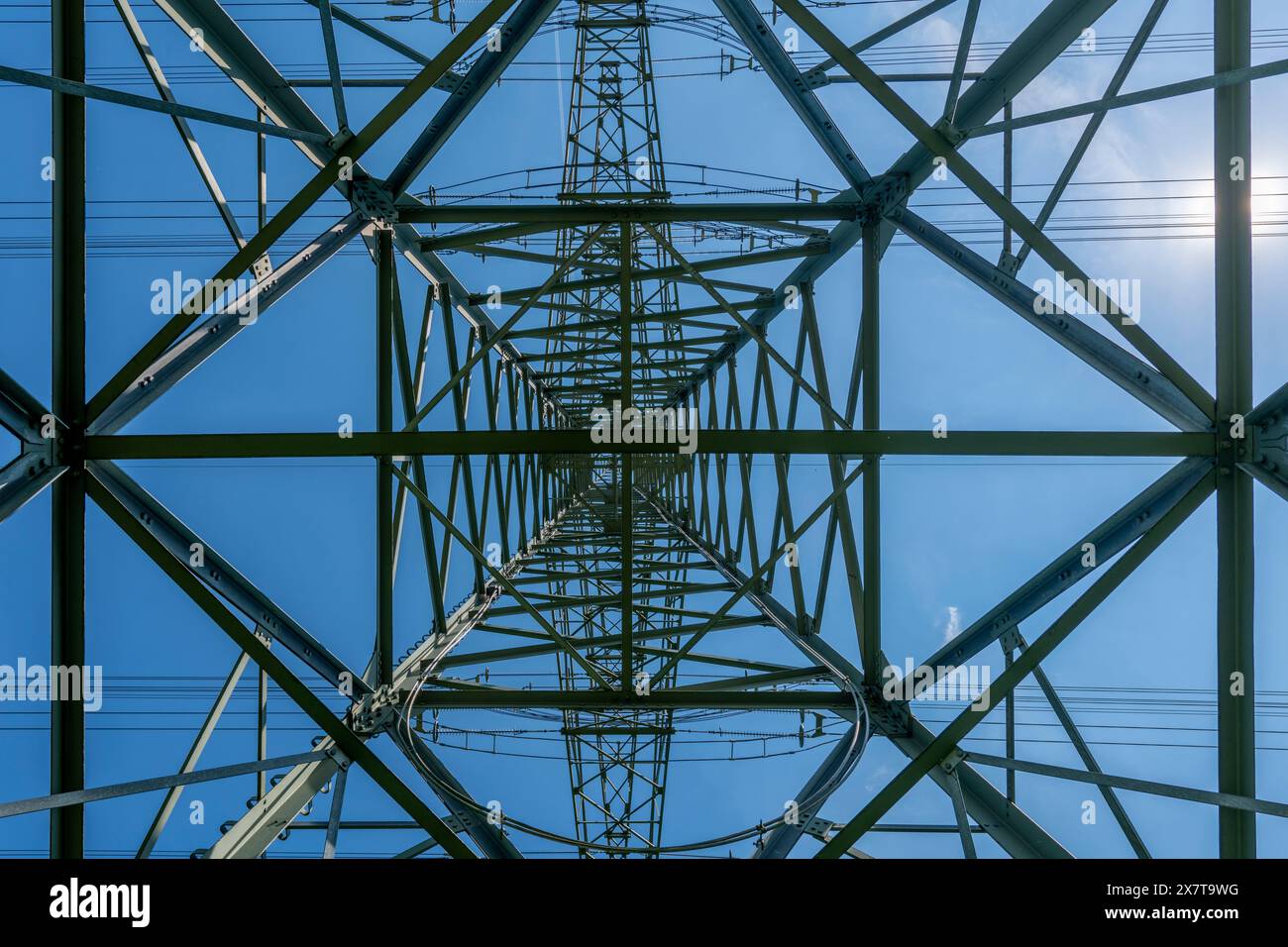 Una grande torre di linea elettrica con una struttura simmetrica, caratterizzata da più linee elettriche e un cielo blu sullo sfondo. Il design della torre è visivo Foto Stock