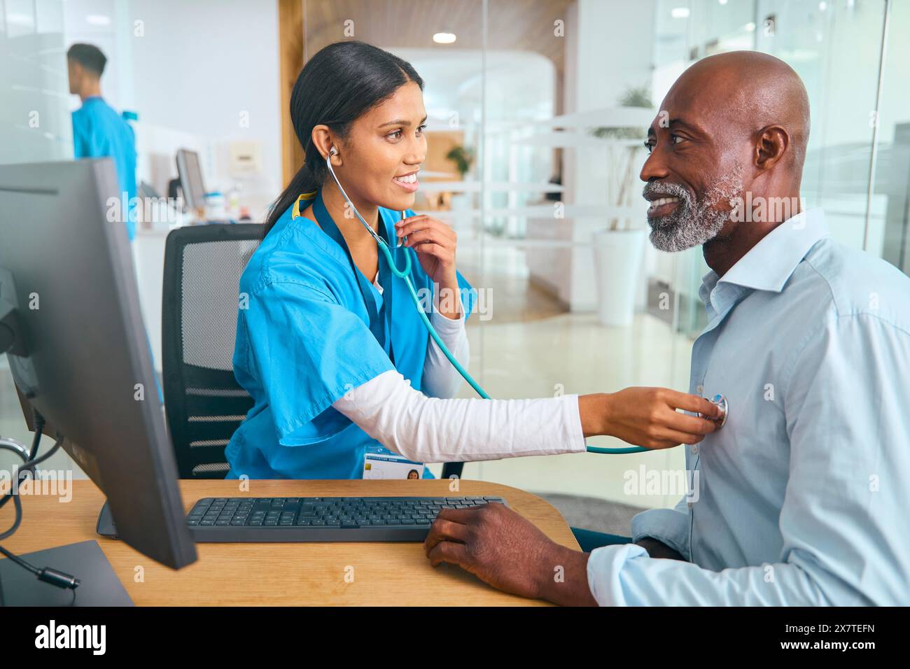 Infermiera o medico che indossa scrub che esamina l'uomo maturo utilizzando lo stetoscopio Foto Stock