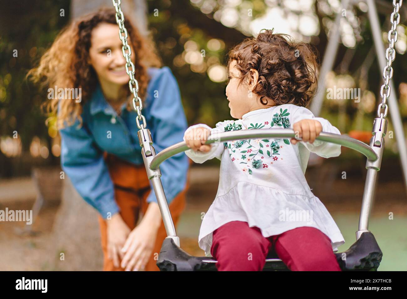Madre e figlia giocano sullo swing, godendo di un momento di gioia in famiglia, sorridendo e divertendosi, all'aperto, felicità e legame in modo naturale Foto Stock