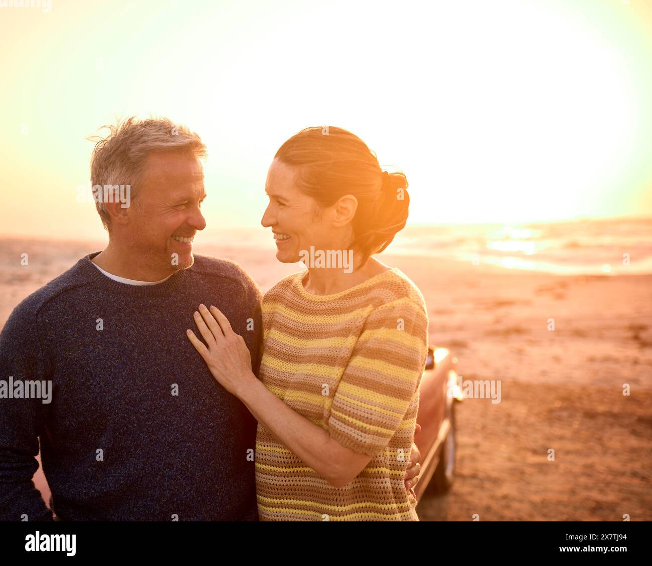 Adorabile coppia senior in pensione in vacanza accanto a Classic Sports Car at Beach Watching Sunrise Foto Stock